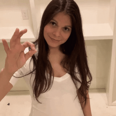 A Woman In A White Shirt Is Smiling And Holding Something In Her Hand GIF