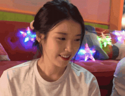 A Woman In A White Shirt Is Smiling In Front Of A Colorful Couch GIF