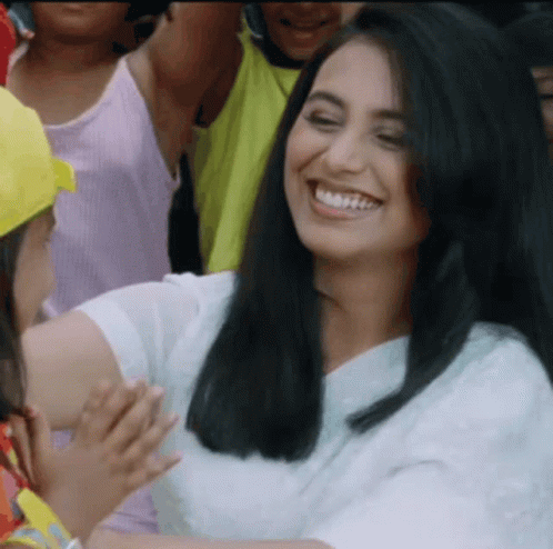 A Woman In A White Shirt Is Smiling In Front Of A Crowd Of People GIF
