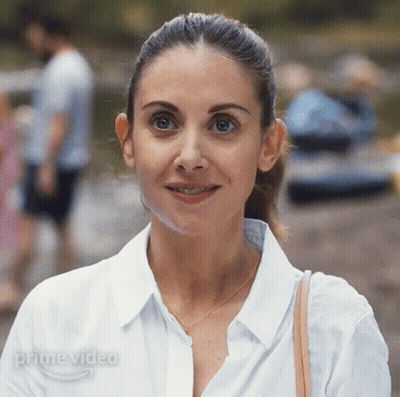 A Woman In A White Shirt Is Smiling In Front Of A Sign That Says Prime Video On It GIF