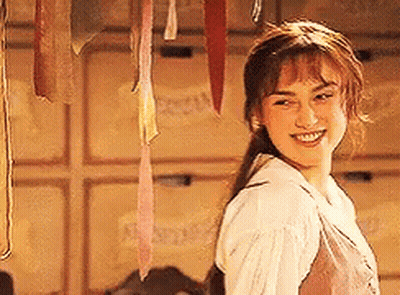A Woman In A White Shirt Is Smiling In Front Of A Wall With Ribbons Hanging From It . GIF