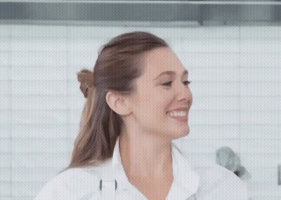 A Woman In A White Shirt Is Smiling In Front Of A White Tiled Wall . GIF