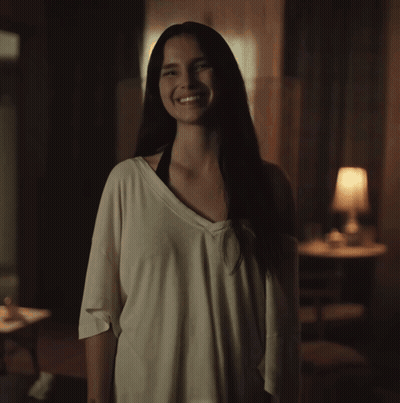 A Woman In A White Shirt Is Smiling In The Dark GIF