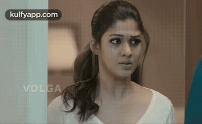 A Woman In A White Shirt Is Standing In Front Of A Glass Door Looking At The Camera . GIF