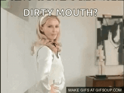 A Woman In A White Shirt Is Standing In Front Of A Wall With The Words `` Dirty Mouth '' Written On It . GIF