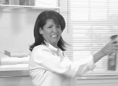 A Woman In A White Shirt Is Standing In Front Of A Window Holding A Bottle . GIF