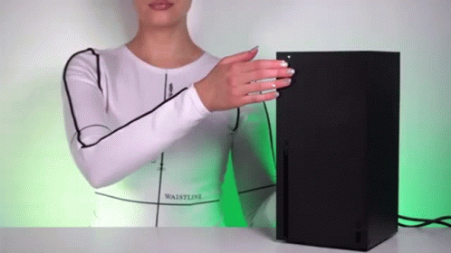 A Woman In A White Shirt Is Standing Next To A Black Xbox Console . GIF