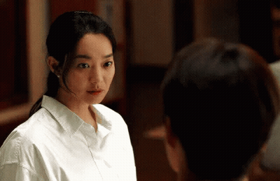 A Woman In A White Shirt Is Standing Next To A Man And Looking At Him . GIF