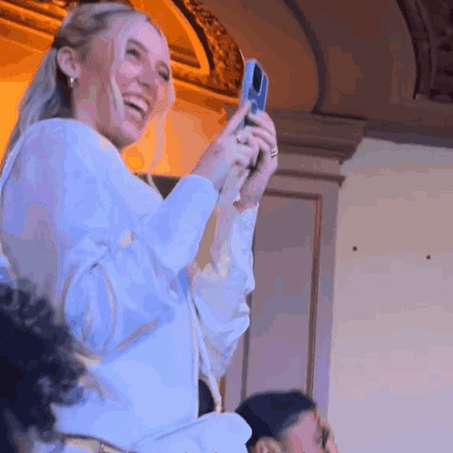 A Woman In A White Shirt Is Taking A Picture With A Cell Phone GIF