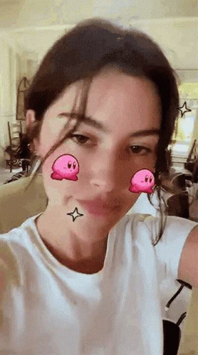 A Woman In A White Shirt Is Taking A Selfie With A Kirby Filter On Her Face . GIF