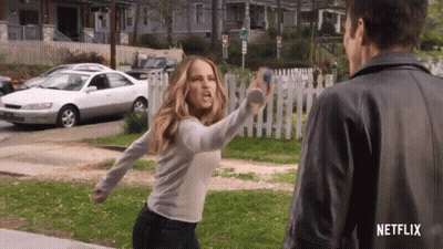 A Woman In A White Shirt Is Throwing A Bottle At A Man In A Leather Jacket . GIF