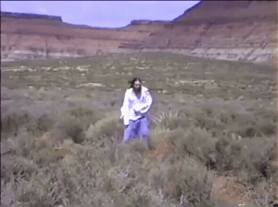 A Woman In A White Shirt Is Walking Through A Field Of Tall Grass . GIF
