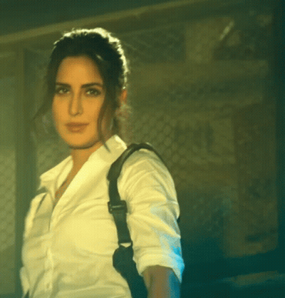 A Woman In A White Shirt With A Black Strap On Her Back GIF