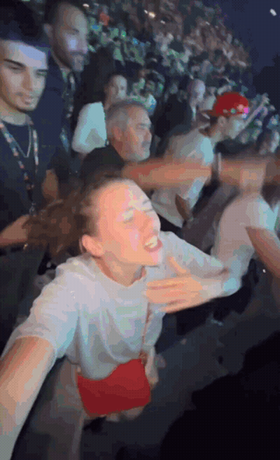 A Woman In A White Shirt With A Red Purse Is Dancing In A Crowd GIF