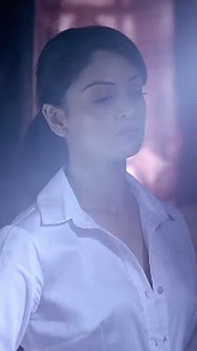 A Woman In A White Shirt With Her Eyes Closed Is Standing In A Dark Room . GIF