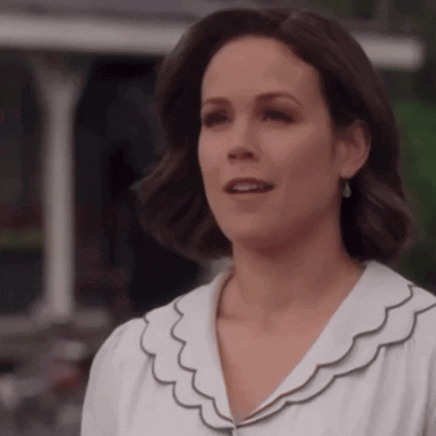 A Woman In A White Shirt With Ruffles On The Collar Is Looking At The Camera . GIF