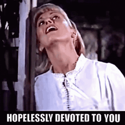 A Woman In A White Shirt With The Words Hopelessly Devoted To You Below Her GIF