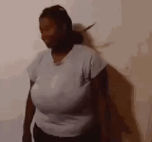 A Woman In A White Shirt With Very Large Breasts Is Standing In Front Of A Wall . GIF