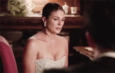 A Woman In A White Strapless Dress Is Sitting Next To A Man In A Suit . GIF