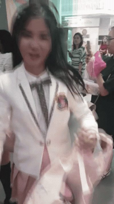 A Woman In A White Suit And Tie Is Holding A Pink Balloon GIF