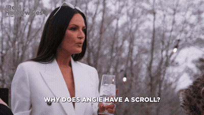 A Woman In A White Suit Is Holding A Glass Of Water And Says Why Does Angie Have A Scroll GIF