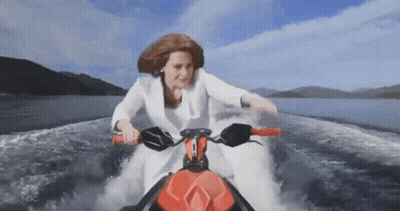 A Woman In A White Suit Is Riding A Jet Ski In The Water GIF
