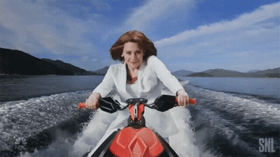 A Woman In A White Suit Is Riding A Jet Ski With The Nbc Logo Behind Her GIF