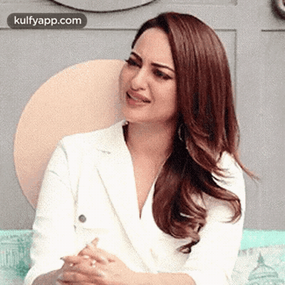 A Woman In A White Suit Is Sitting On A Couch With Her Hands Folded . GIF