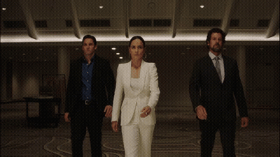 A Woman In A White Suit Is Standing In Between Two Men In Suits GIF
