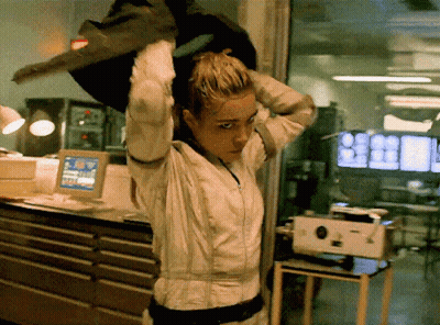 A Woman In A White Suit Is Standing In Front Of A Computer Monitor GIF