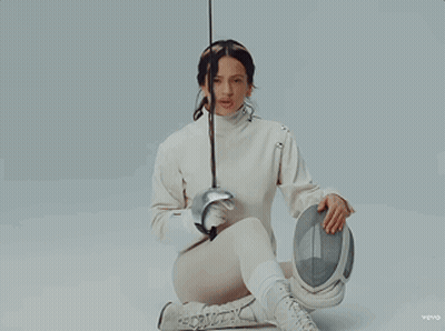 A Woman In A White Sweater Is Holding A Fencing Sword GIF
