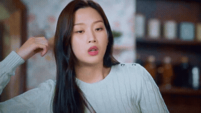 A Woman In A White Sweater Is Holding Her Hair And Making A Funny Face GIF