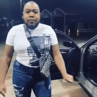A Woman In A White T-Shirt And Jeans Is Standing In Front Of A Car . GIF