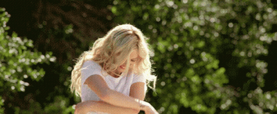 A Woman In A White T-Shirt Is Standing In Front Of Trees GIF
