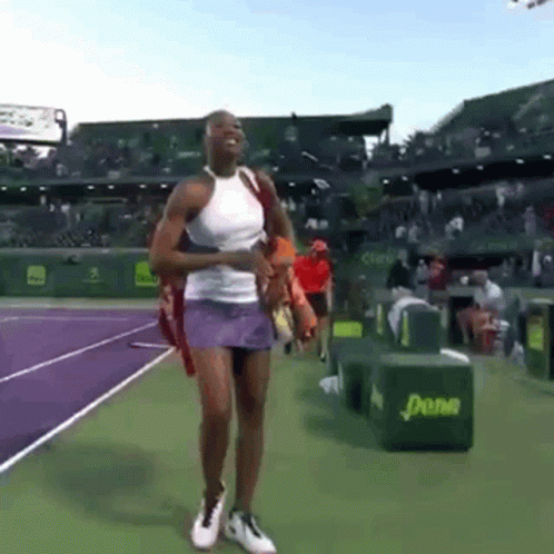 A Woman In A White Tank Top And Purple Skirt Is Walking On A Tennis Court .. GIF