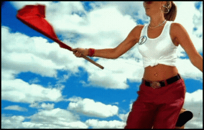 A Woman In A White Tank Top And Red Pants Holds A Red Flag GIF