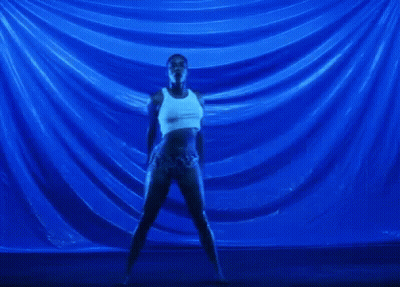 A Woman In A White Tank Top And Shorts Is Dancing In Front Of A Blue Background . GIF