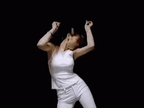 A Woman In A White Tank Top And White Pants Is Dancing With Her Arms In The Air . GIF