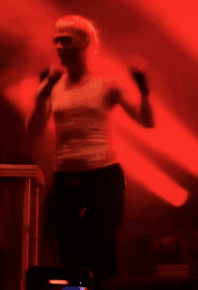 A Woman In A White Tank Top Is Dancing In A Dark Room GIF
