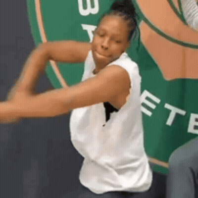 A Woman In A White Tank Top Is Dancing In Front Of A Sign That Says Boston GIF