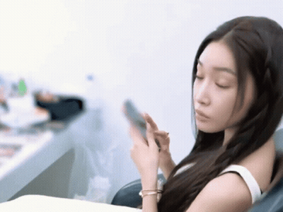 A Woman In A White Tank Top Is Looking At Her Phone GIF