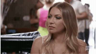 A Woman In A White Tank Top Is Sitting In A Room With A Group Of People . GIF