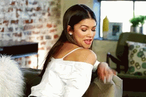 A Woman In A White Tank Top Is Sitting On A Couch With Her Tongue Out . GIF