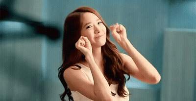 A Woman In A White Tank Top Is Smiling And Making A Heart Shape With Her Hands GIF