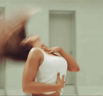 A Woman In A White Tank Top Is Standing In A Room GIF