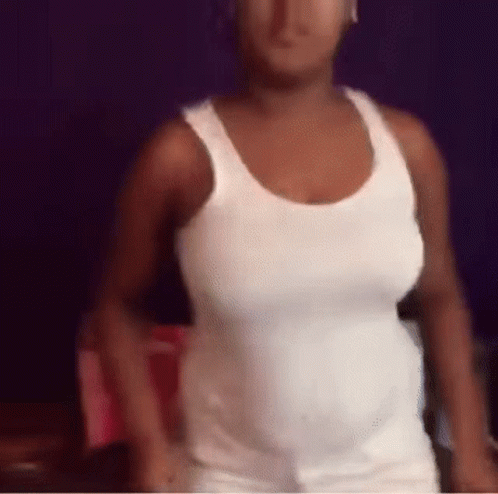A Woman In A White Tank Top Is Standing In A Room . GIF