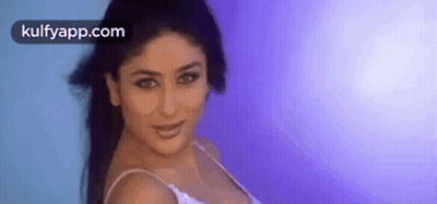 A Woman In A White Tank Top Is Standing In Front Of A Blue Wall . GIF