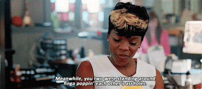 A Woman In A White Tank Top Is Standing In Front Of A Computer And Talking To Another Woman . GIF