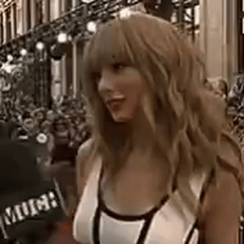 A Woman In A White Tank Top Is Standing In Front Of A Crowd Of People . GIF