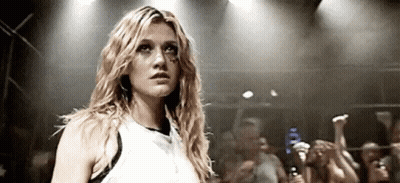 A Woman In A White Tank Top Is Standing In Front Of A Crowd Of People . GIF